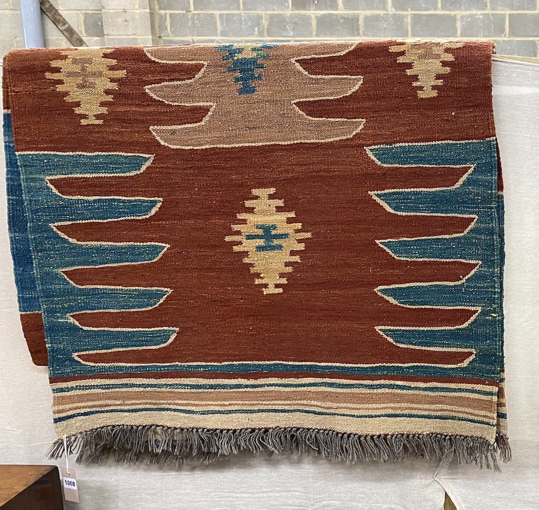 A Kilim runner with geometric motifs on a brick red ground, 384 x 85cm